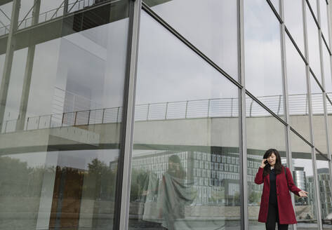 Geschäftsfrau steht in der Nähe eines modernen Gebäudes und benutzt ein Smartphone - AHSF01523
