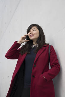 Porträt einer modernen Geschäftsfrau mit Smartphone vor einer Wand - AHSF01534