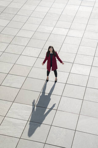 Blick von oben auf eine gehende moderne Geschäftsfrau, die mit ausgebreiteten Armen auf dem Betonboden steht, lizenzfreies Stockfoto