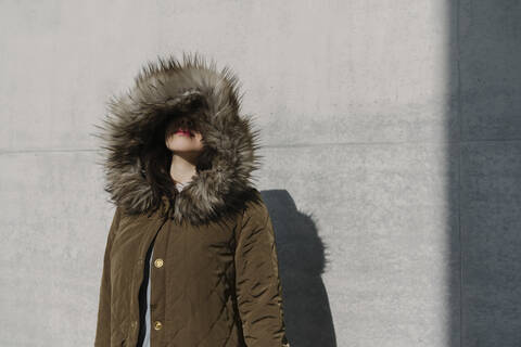 Porträt einer anonymen Frau mit Wintermantel vor dem Hintergrund einer Mauer, lizenzfreies Stockfoto