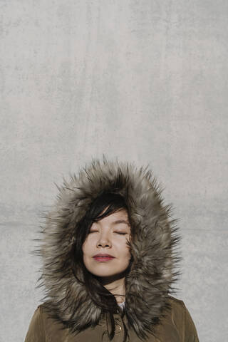 Porträt einer Frau im Wintermantel vor dem Hintergrund einer Mauer, lizenzfreies Stockfoto