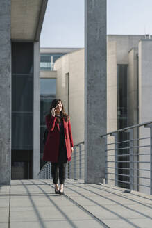 Geschäftsfrau zu Fuß auf einer Brücke in der Nähe von modernen Gebäude und mit Smartphone - AHSF01554