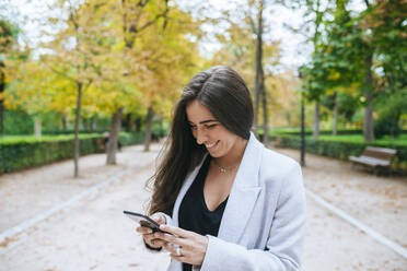 Lächelnde Frau mit Smartphone im Park - KIJF02827