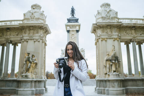 Lächelnde Frau mit einer Kamera vor dem Alfonso XII-Denkmal im El Retiro-Park, Madrid, Spanien, lizenzfreies Stockfoto