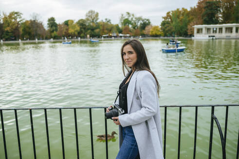 Frau mit Kamera an einem See im El Retiro Park, Madrid, Spanien - KIJF02833