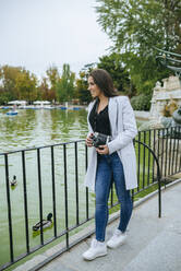 Frau mit Kamera an einem See im El Retiro Park, Madrid, Spanien - KIJF02834