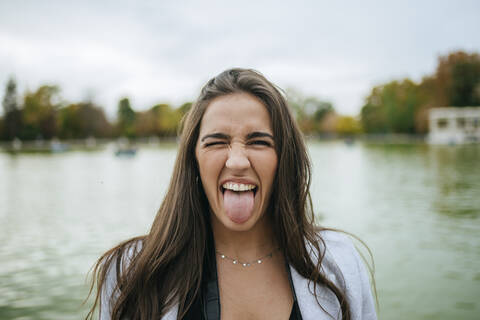 Porträt einer Frau an einem See, die ihre Zunge herausstreckt, lizenzfreies Stockfoto
