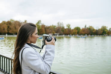 Woman standing at a lake taking a photo - KIJF02837