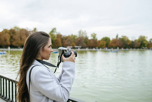 Frau steht an einem See und macht ein Foto - KIJF02837