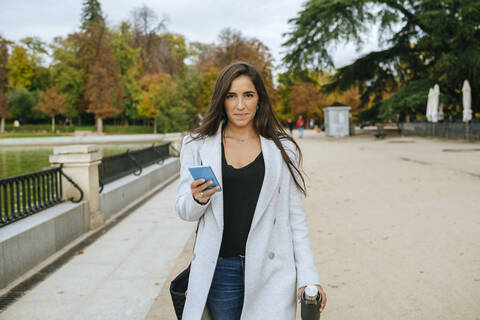 Frau geht durch einen Park und hält ihr Smartphone in der Hand, lizenzfreies Stockfoto