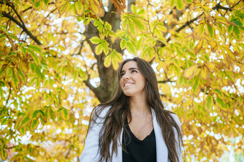 Lächelnde Frau unter herbstlichem Baum stehend, lizenzfreies Stockfoto