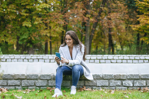 Lächelnde Frau benutzt ihr Smartphone in einem Park - KIJF02845