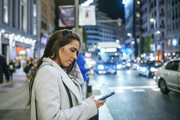 Frau benutzt nachts ihr Smartphone auf der Straße - KIJF02850