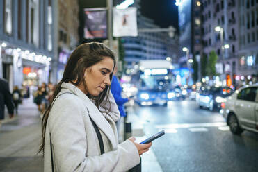 Woman using her smartphone in the street at night - KIJF02850
