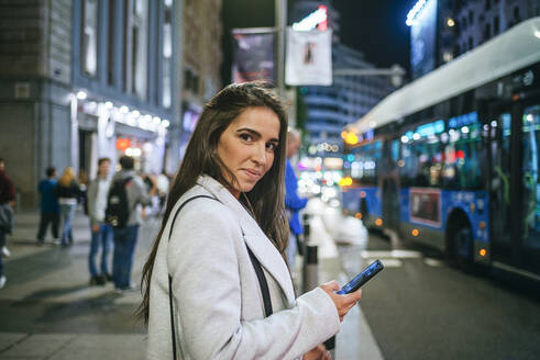 Frau benutzt nachts ihr Smartphone auf der Straße - KIJF02851