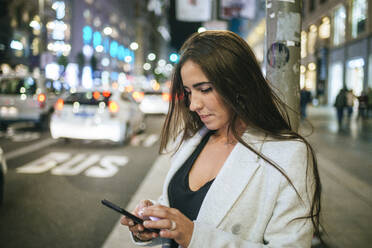 Frau benutzt nachts ihr Smartphone auf der Straße - KIJF02853
