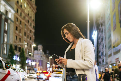 Frau benutzt nachts ihr Smartphone auf der Straße - KIJF02855