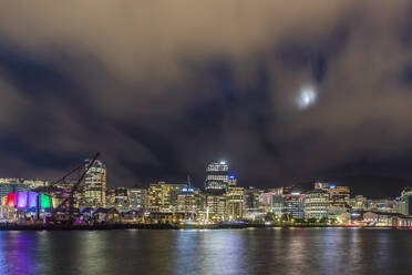 New Zealand, Wellington, Clouds over illuminated waterfront city skyline at night - FOF11264