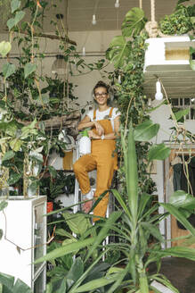 Portrait of a young woman standing on a ladder in a small gardening shop - VPIF01844