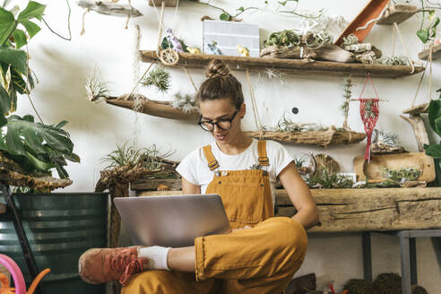 Young woman using laptop in a small gardening shop - VPIF01849