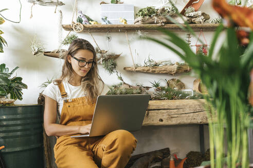 Young woman using laptop in a small gardening shop - VPIF01853