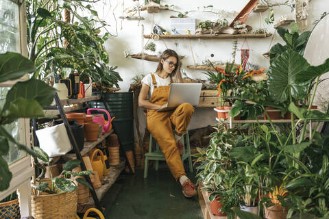 Junge Frau mit Laptop in einer kleinen Gärtnerei, lizenzfreies Stockfoto