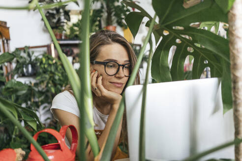 Young woman using laptop surrounded by plants - VPIF01855