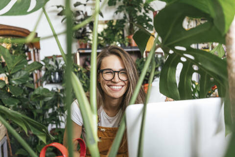 Porträt einer glücklichen jungen Frau mit Laptop, umgeben von Pflanzen, lizenzfreies Stockfoto