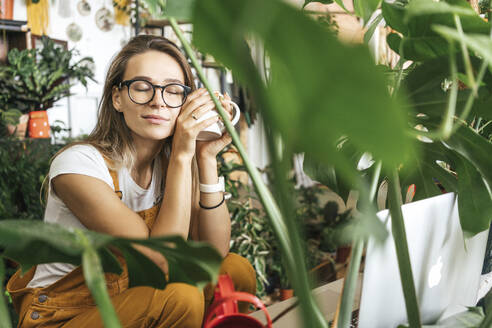 Young woman having a coffee break in a small gardening shop - VPIF01857