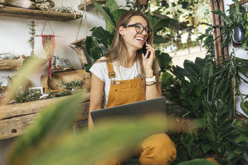 Laughing young woman on the phone in a small gardening shop - VPIF01860