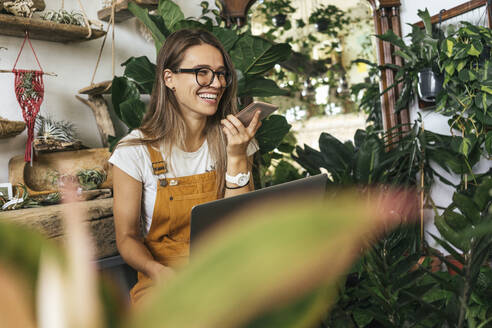 Happy young woman using smartphone in a small gardening shop - VPIF01861