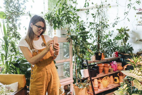 Young woman taking smartphone picture in a small gardening shop - VPIF01868