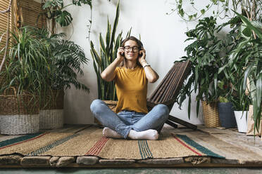 Relaxed young woman sitting on the floor at home listening to music - VPIF01870