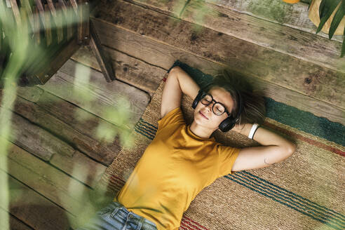 Relaxed young woman lying on the floor at home listening to music - VPIF01872