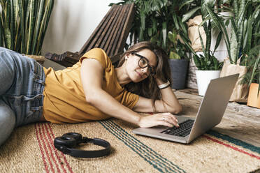 Entspannte junge Frau, die zu Hause auf dem Boden liegt und einen Laptop benutzt - VPIF01873