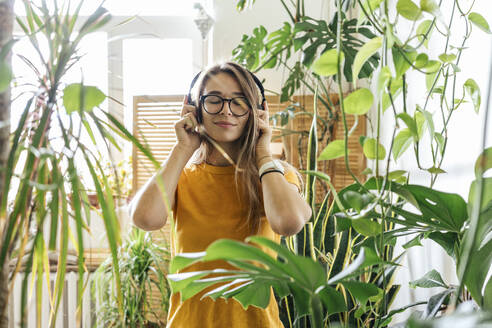 Young woman surrounded by plants listening to music with headphones - VPIF01875