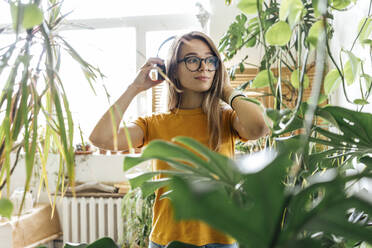 Junge Frau umgeben von Pflanzen, die mit Kopfhörern Musik hören - VPIF01876
