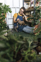 Young woman with dinosaur figurine sitting on the floor in a small shop with plants - VPIF01887