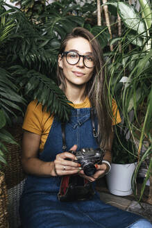 Portrait of a young woman with a camera in a small gardening shop - VPIF01891