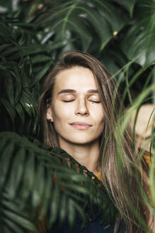 Portrait of a young woman with closed eyes amidst green plants - VPIF01893