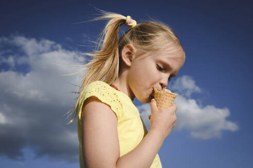 Porträt eines blonden Mädchens, das Eis gegen den Himmel isst - EYAF00709