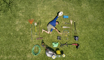 Blick von oben auf einen Gärtner im Gras liegend mit allen Werkzeugen, die er für die Pflege des Gartens benötigt - VEGF00987