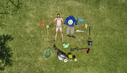 Blick von oben auf einen Gärtner im Gras liegend mit allen Werkzeugen, die er für die Pflege des Gartens benötigt - VEGF00990