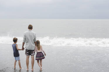 Rückenansicht eines Mannes, der Hand in Hand mit seiner kleinen Tochter und seinem Sohn an der Strandpromenade steht - EYAF00720