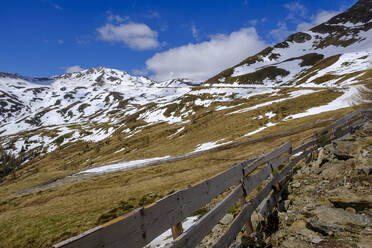 Italien, Südtirol, Einfacher Holzzaun am Penser Joch mit Schneeschmelze im Hintergrund - LBF02822