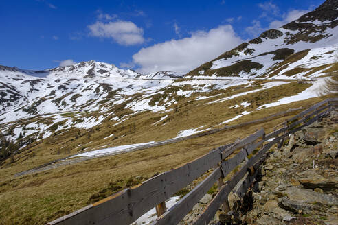 Italien, Südtirol, Einfacher Holzzaun am Penser Joch mit Schneeschmelze im Hintergrund - LBF02822