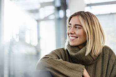 Smiling young woman sitting in waiting area looking around - DIGF08964