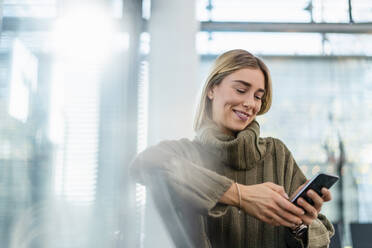 Smiling young woman sitting in waiting area using cell phone - DIGF08966