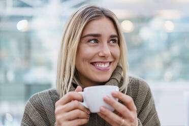 Porträt einer lächelnden jungen Frau, die eine Tasse Kaffee hält und wegschaut - DIGF08972
