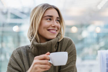Porträt einer lächelnden jungen Frau, die eine Tasse Kaffee hält und wegschaut - DIGF08973